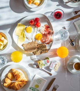 Hearty breakfast with eggs, cheese, ham, muesli, juice, croissant, and fruit on a set table.
